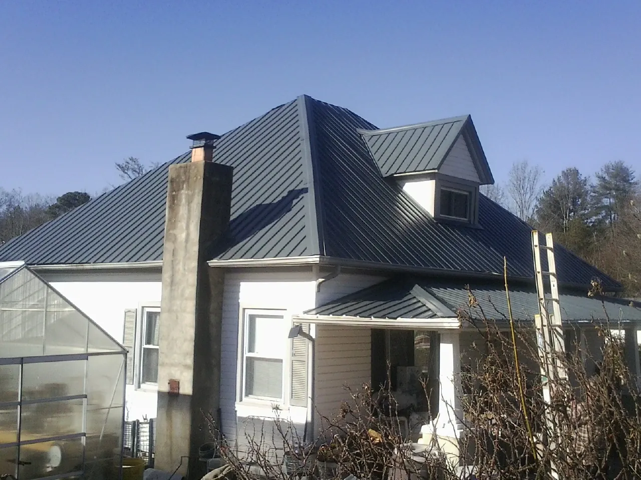 Dark blue standing seam metal roof on a white farmhouse with dormer — Slate & Tile Roof Repair by Roofing Brothers in Lake Odessa