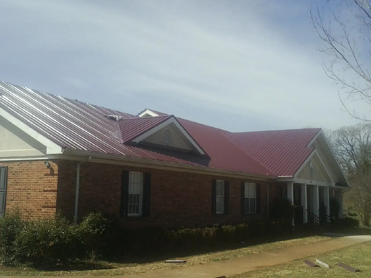Red metal roof with gabled entries on a long brick building, from a Hail Damage Roof Repair job in Lake Odessa