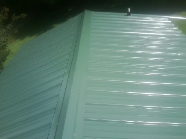 New green metal panels meeting at the ridge of a roof — Flat Roof Repair work by our crew in Lake Odessa
