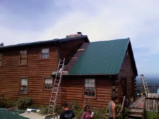 Green metal roof going on a two story log home with ladders set in Lake Odessa