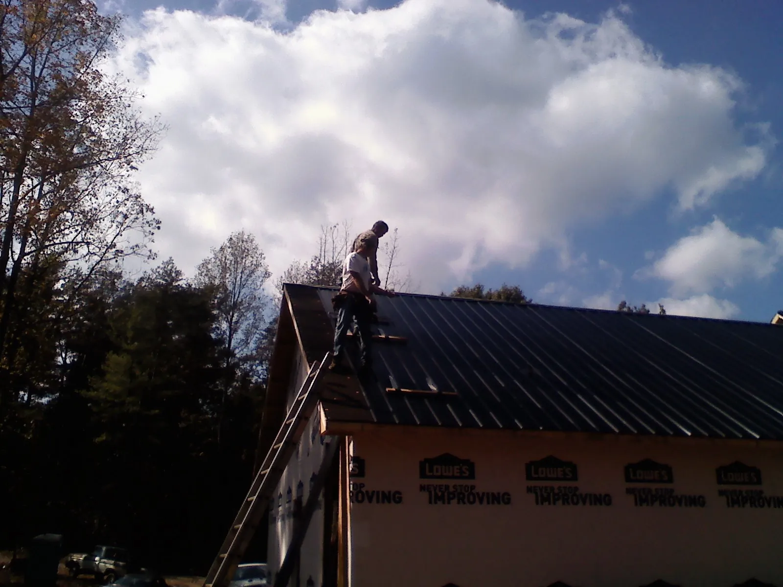 Roofer fastening dark metal panels high against a cloudy sky, from a Roof Inspection job in Lake Odessa