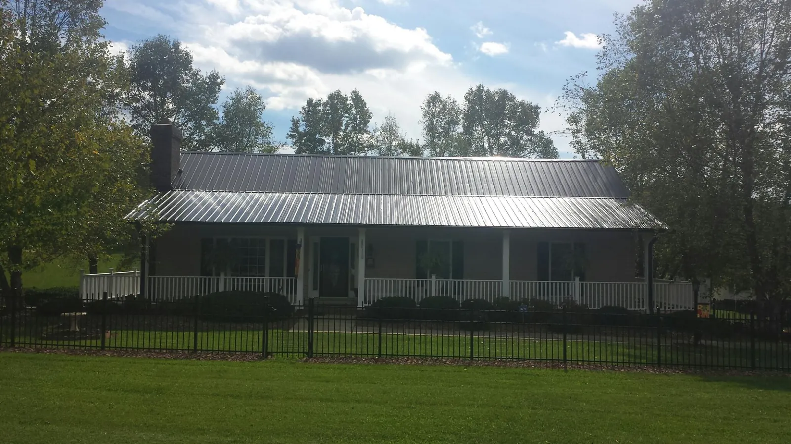 Gray metal roof on a brick ranch with a full width front porch — Gutter Guard Installation work by our crew in Lake Odessa