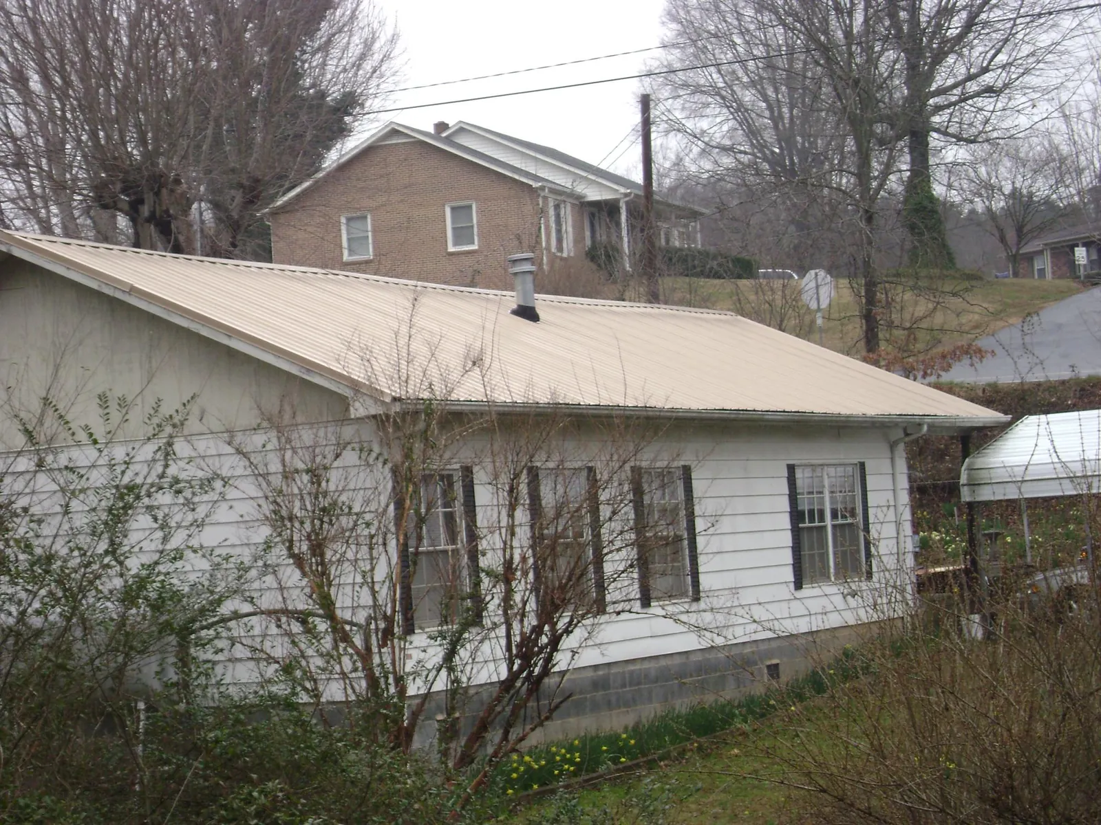 Tan metal roof on a white sided house set into a hillside — Commercial Roofing by Roofing Brothers in Lake Odessa