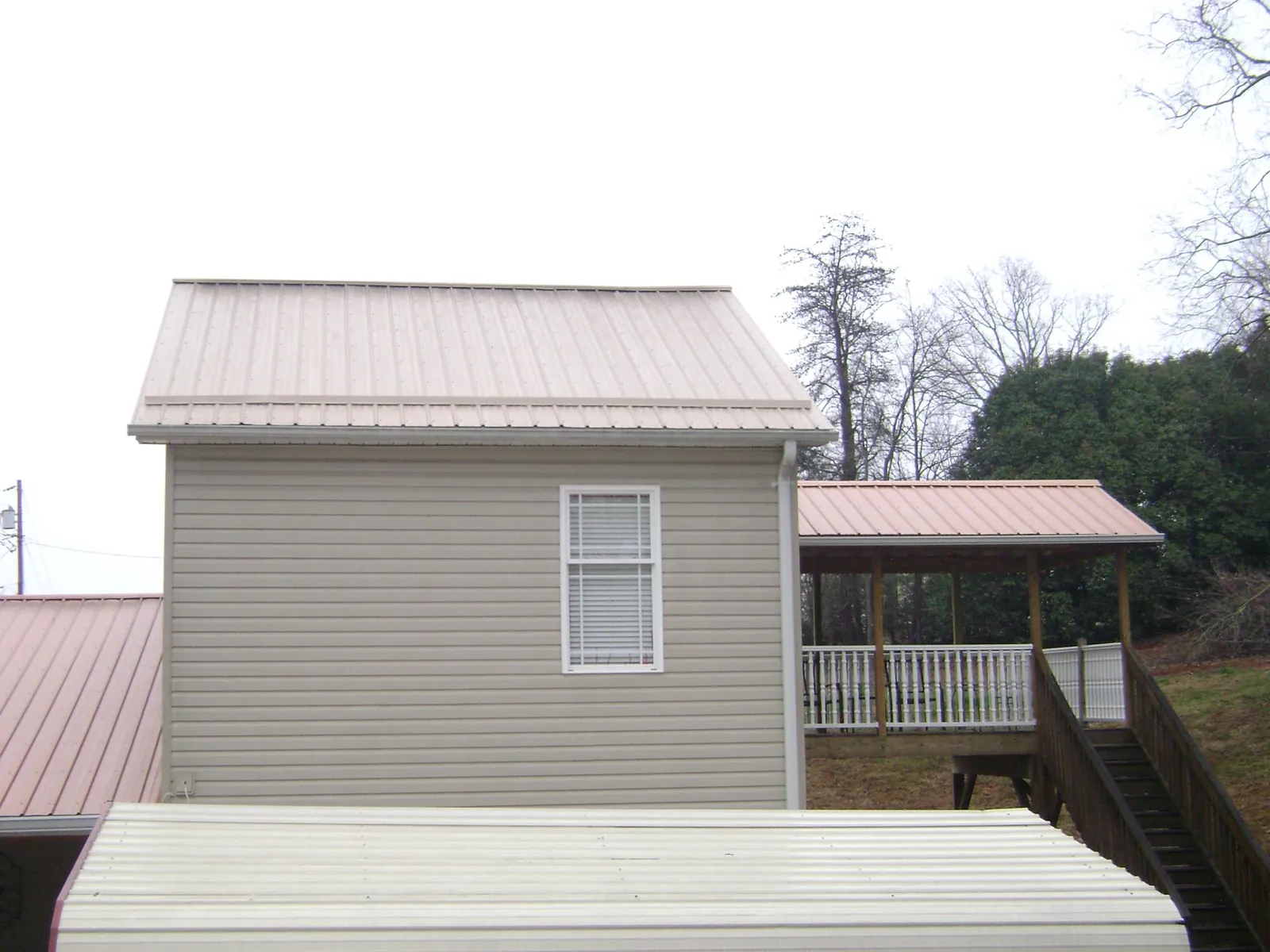 Tan metal roofs on a two story addition and attached porch, from a Roof Replacement job in Lake Odessa
